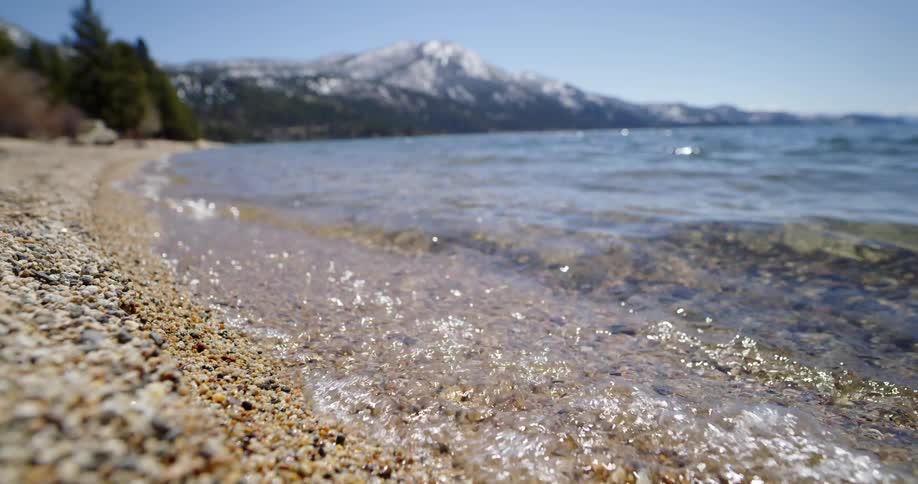 Water from a lake washes onto a gravel beach on a sunny day