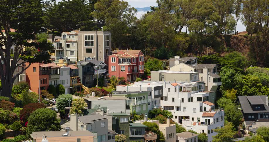 A neighborhood of multistory buildings and trees on a hill on a sunny day