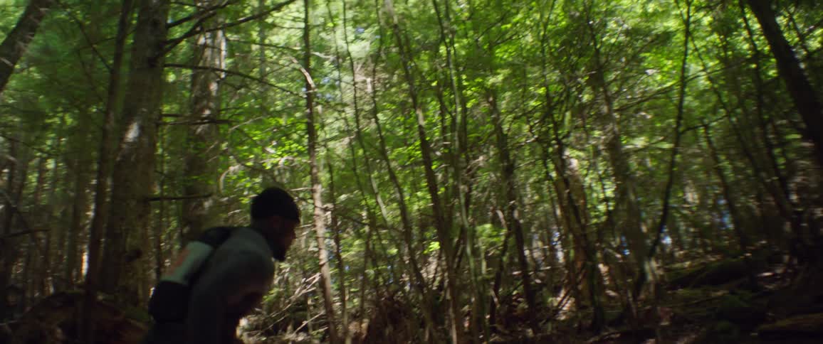 A male athlete is running up a dirt trail in a forest