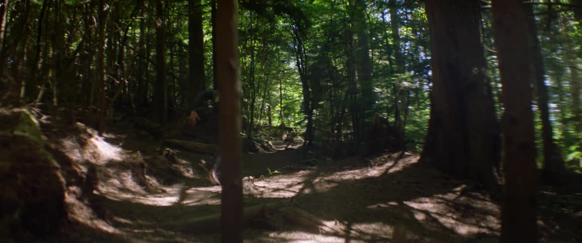 A male athlete runs up a dirt trail in a forest during the day