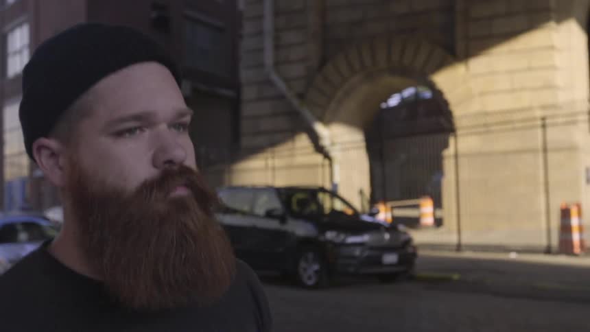 A man with a beard walks down a city street during the day