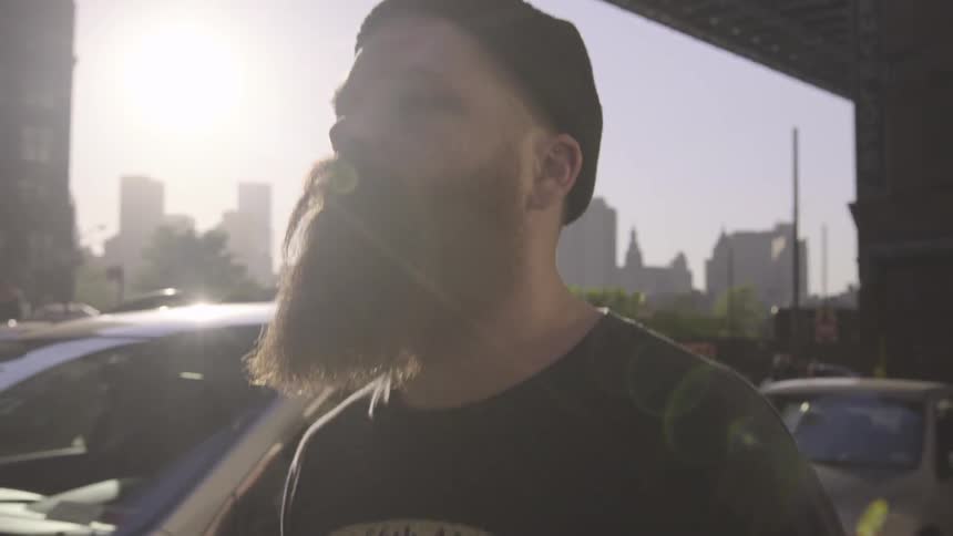 A bearded man walks down a street on a cloudy day