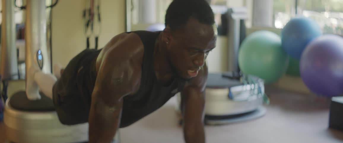 A male athlete is doing pushups while balanced on dumbbells