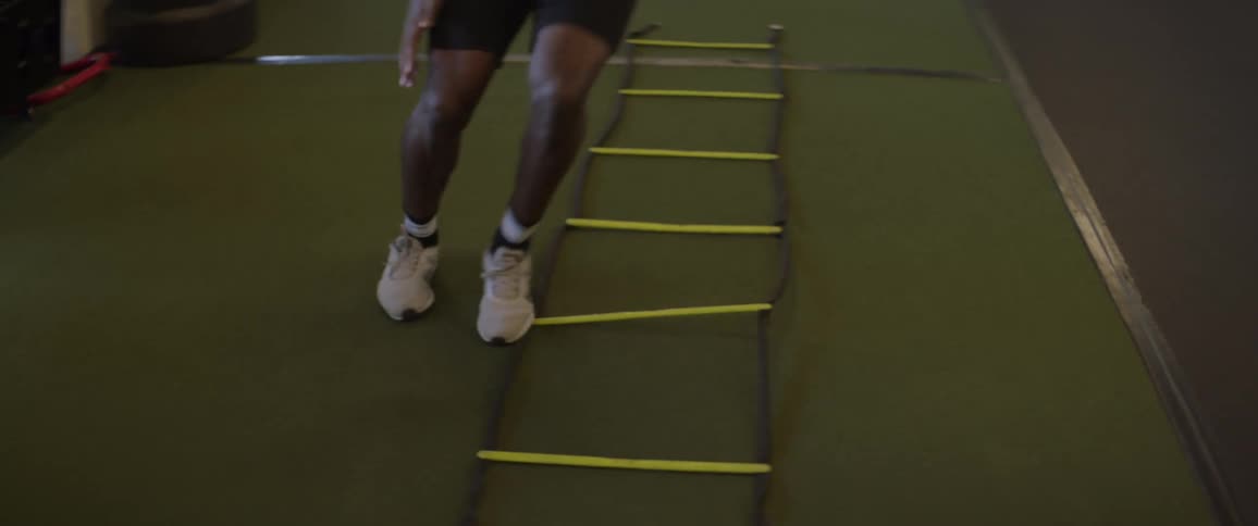 A male athlete is training footwork using a ladder rope in a gym