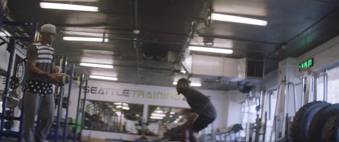 Two people work out with a football in the gym
