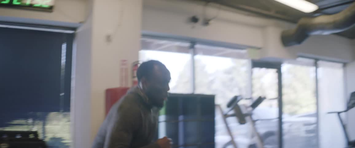 A man is running laps and catching a football in a gym