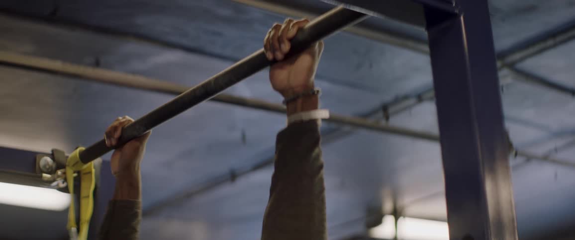 A sweaty man grabs a metal bar in the gym and does pull ups