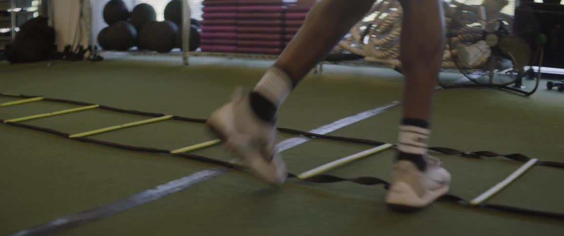 An athlete runs through an agility ladder in a gym