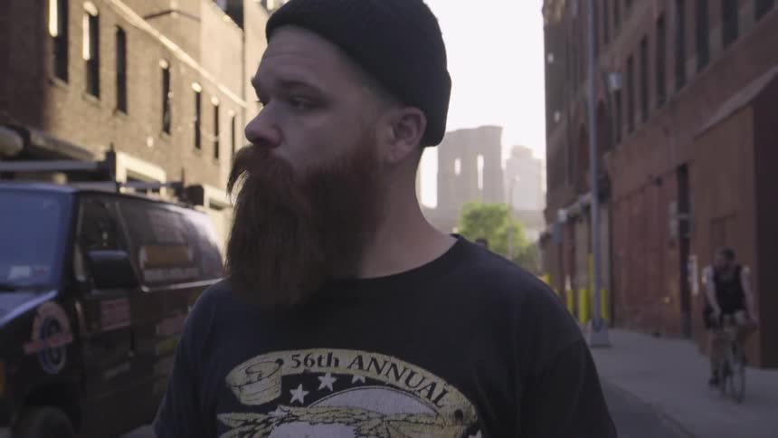 Bearded man walking down a city street with two cyclists not far behind