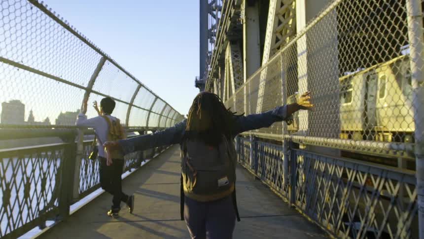 A woman is walking over a bridge with her arms outstretched