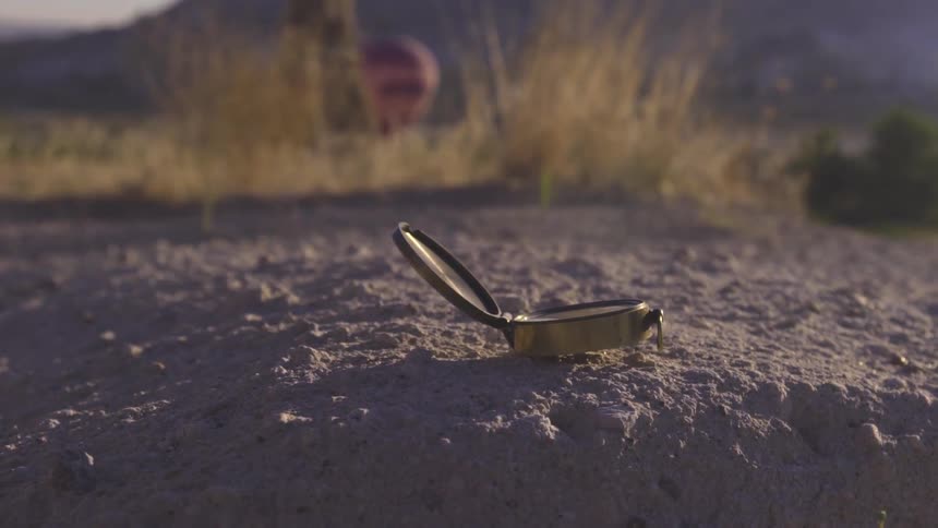 Close up of a compass on the ground as person walks off in the distance