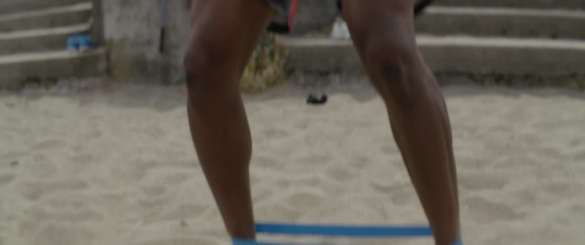 A man is exercising on the beach with a rubber band