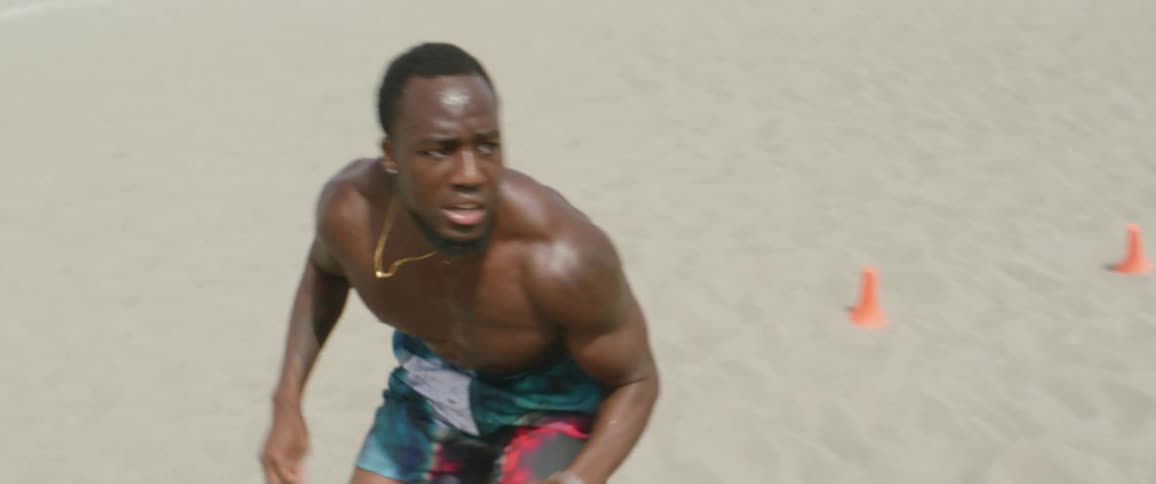 A man crouches and runs off in the sand