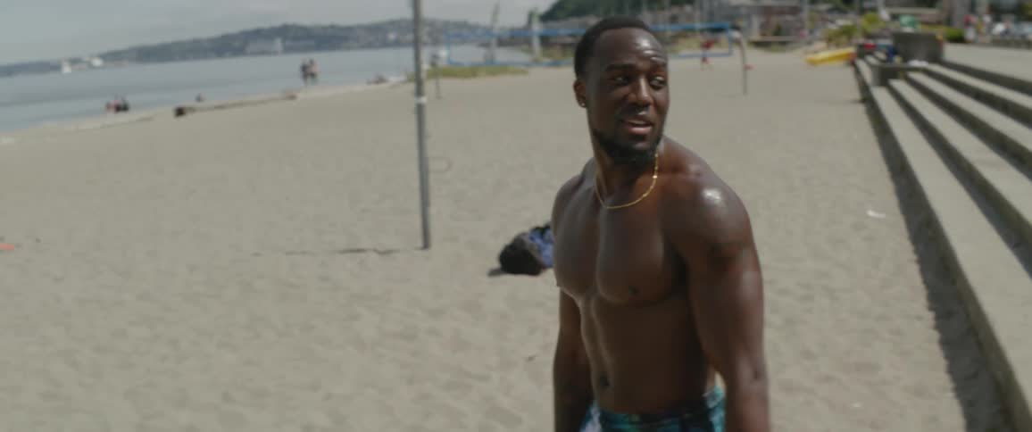 Sweaty shirtless man gets up from stone steps and walks down the beach