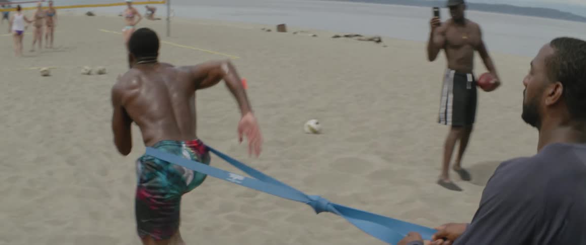 Men are playing football and practicing on the beach