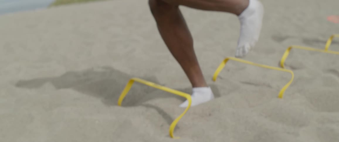 A man is jumping in the sand over obstacles