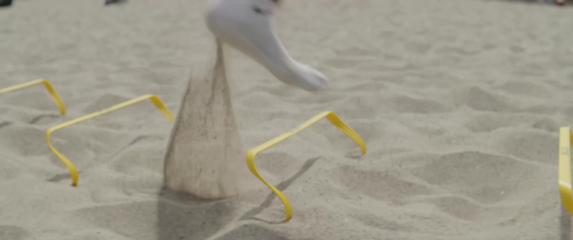 Man hops over small hurdles outside in the sand