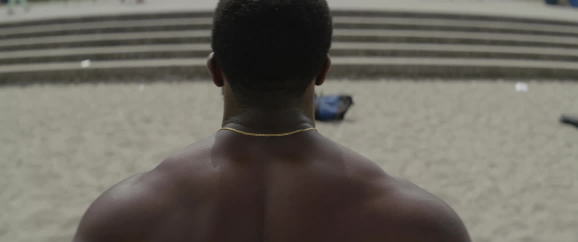 A shirtless man stands on a sandy beach