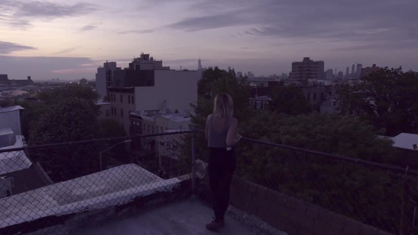 A woman leans over a fence on a rooftop