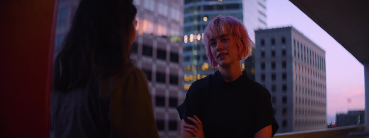 Two young women talking under a red light in a balcony in the city at sunset