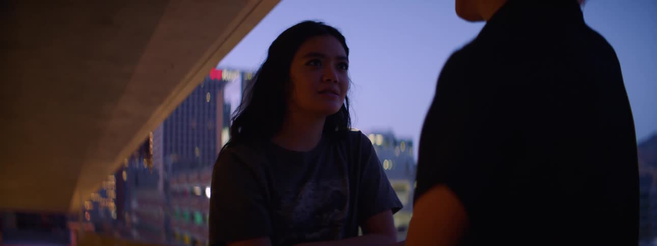 Two teenagers have an argument outside with the city skyline in the background
