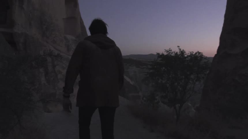 A person is walking outside near a canyon at sunset,