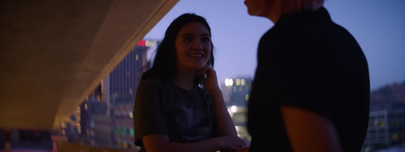 Friends hug and talk on a garage ramp in front of city skyline at night