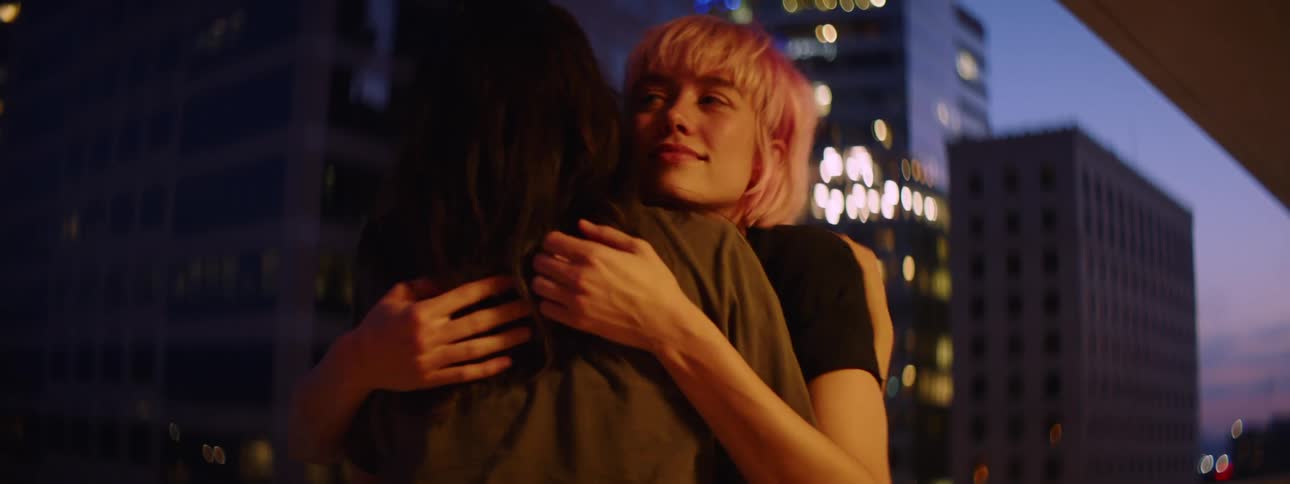 Two teenage girls in a downtown area talk and then hug one another