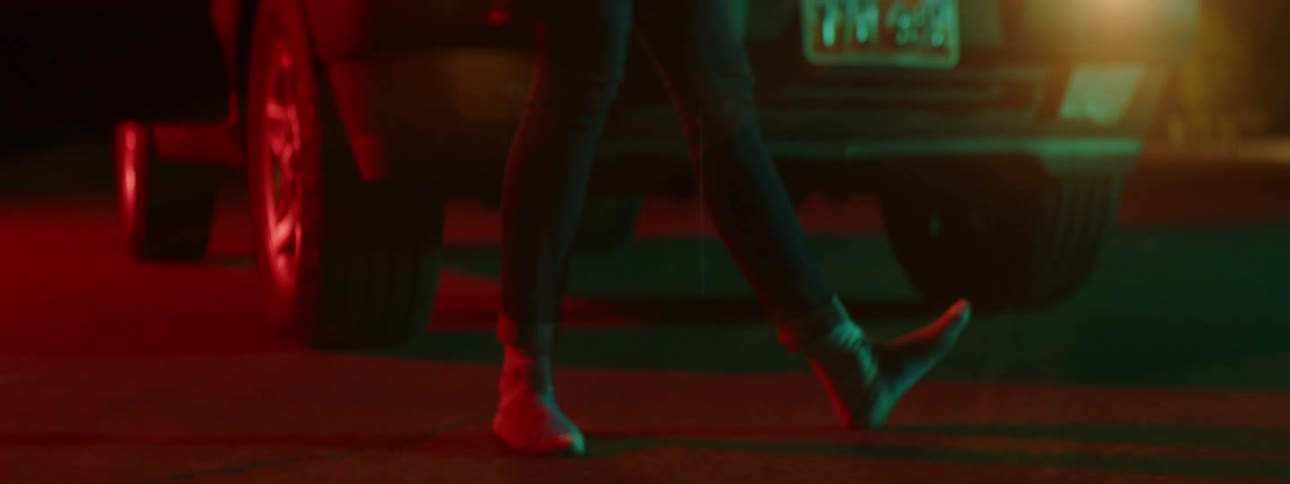 A young female dances outdoors at night in front of an idle vehicle with its headlights turned on