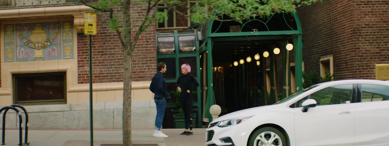 A man and woman appear to be fighting standing on a city sidewalk in front of a building