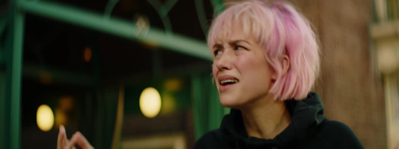 A woman with pink hair arguing with a man and walking away with a building in the background
