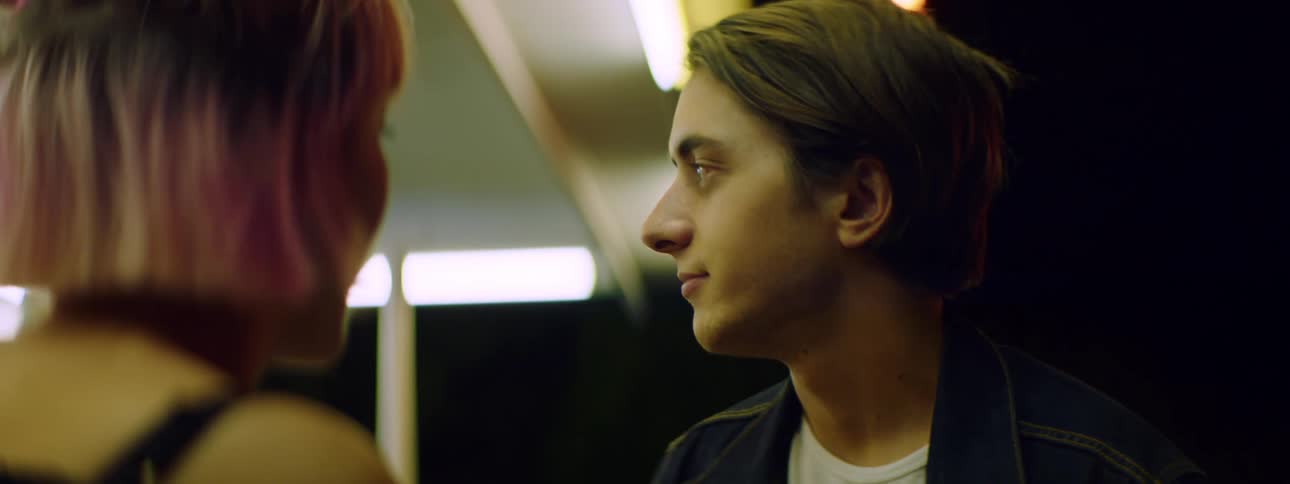 Young couple stands outside at night under store overhang talking and kissing