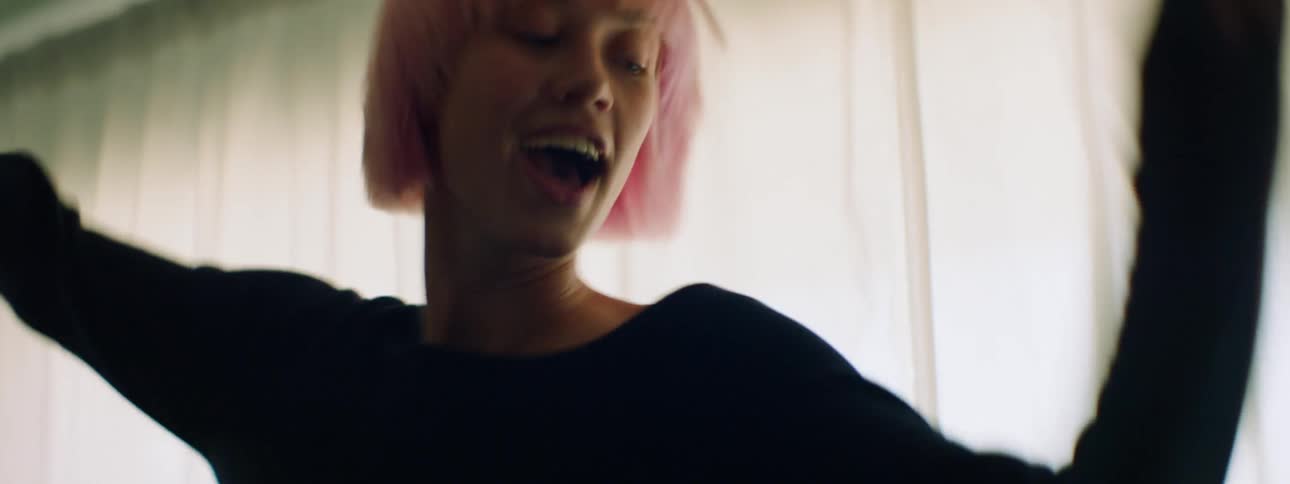 Woman with a long sleeve black t shirt and pink hair dances wildly in a room