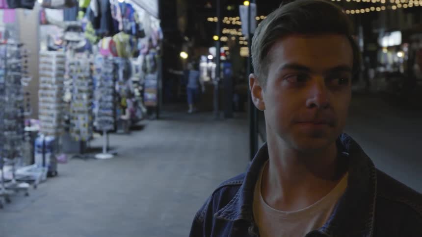 A man stands on on the sidewalk of a city at night