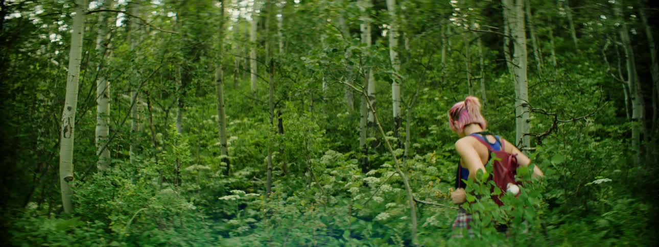 A woman hikes through tall plants in a forest and stops to look around