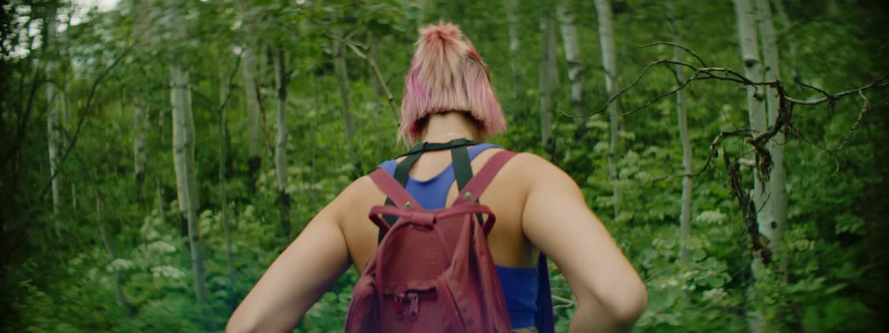 A young woman wearing a backpack carefully makes her way through a densely forested area