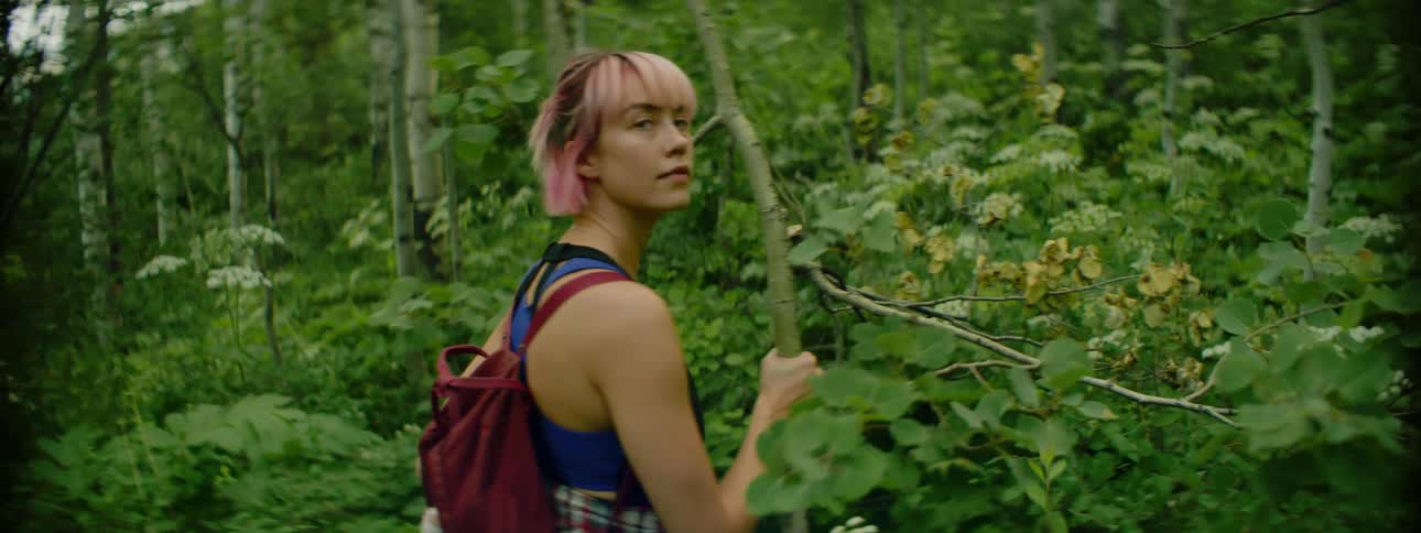 A young woman checks behind her before hiking through the dense vegetation of a forest
