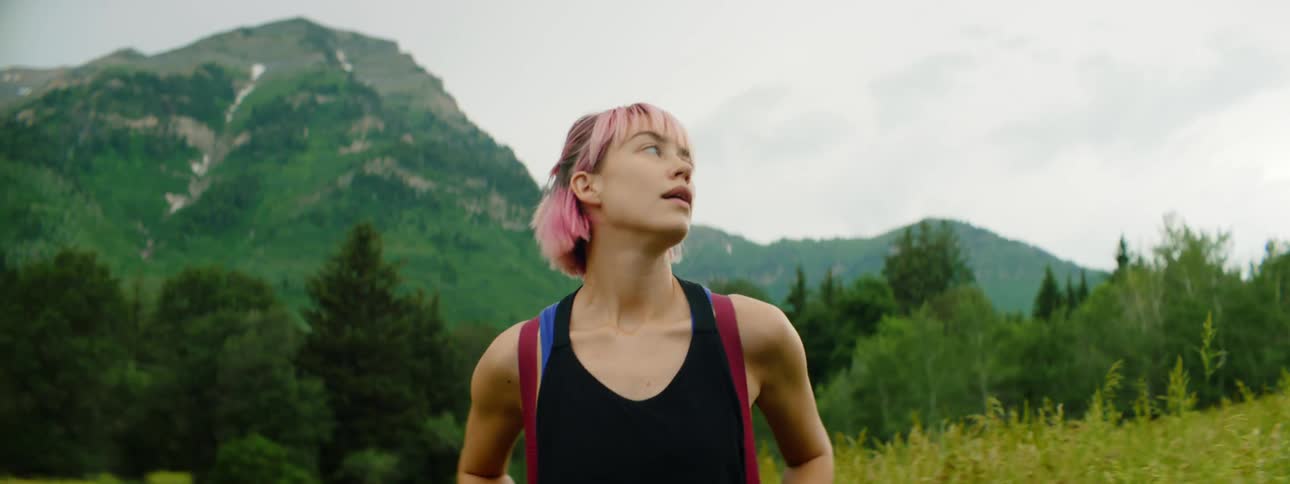 A woman is hiking through the grass towards the mountains