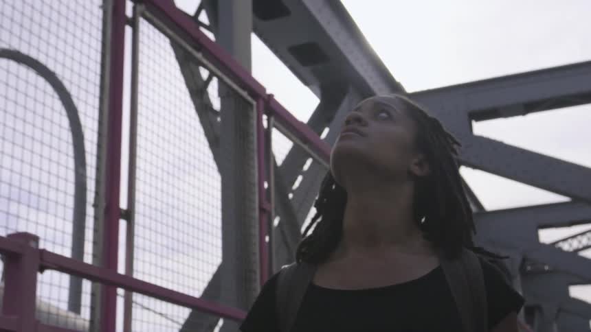 A woman walks across a fenced bridge