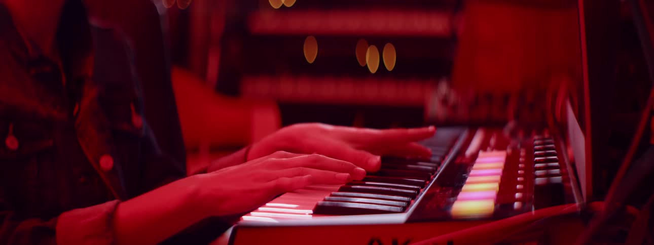 A musician plays an electric musical keyboard in a room illuminated by a red light