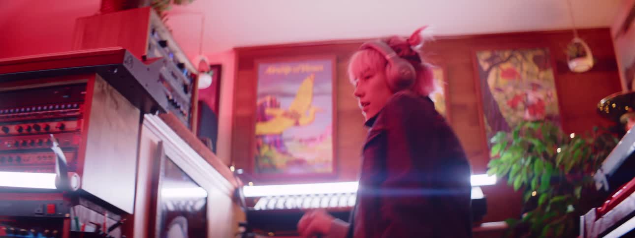 A woman with short blonde hair wears headphones and dances in a music studio