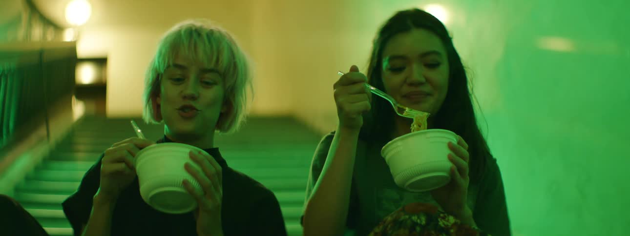 Two women laugh and eat in the stairwell