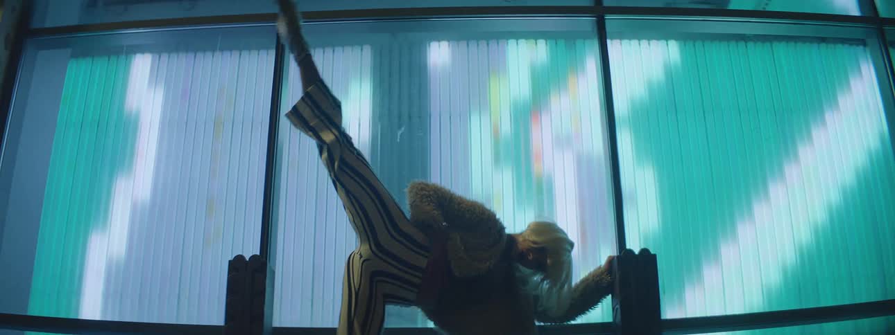 Female dancer with white short hair dances acrobatically in front of screens showing pixelated art