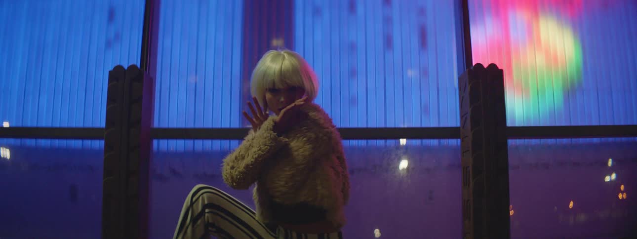 A teenage girl dancing outside in a city as lights flash behind her