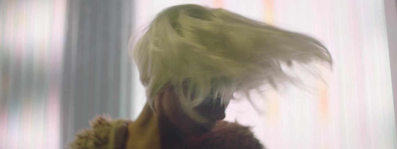Blonde woman wearing faux fur jacket dances against wall tinted with colors