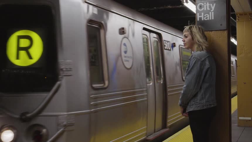 A train enters a subway as a woman waits