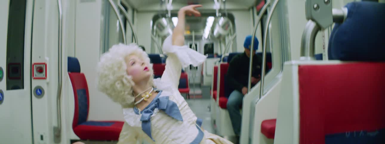 A female in a costume and wig dancing on the subway