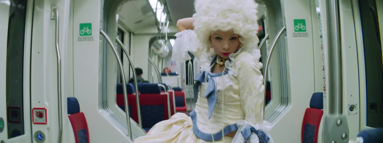 A young woman in a costume and wig dances in the aisle of a subway