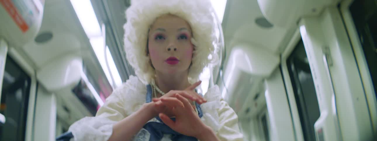 A female in a costume dress and wig dancing on the subway