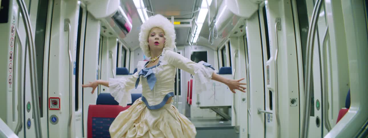 Dancer wearing historical costume and white wig dances in middle of subway car